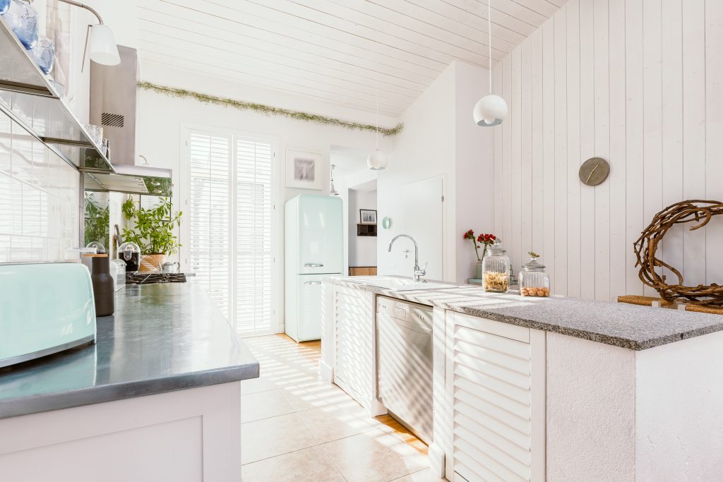 Bright, modern kitchen featuring a light wooden ceiling, white walls, and a stainless steel countertop with an aqua toaster.